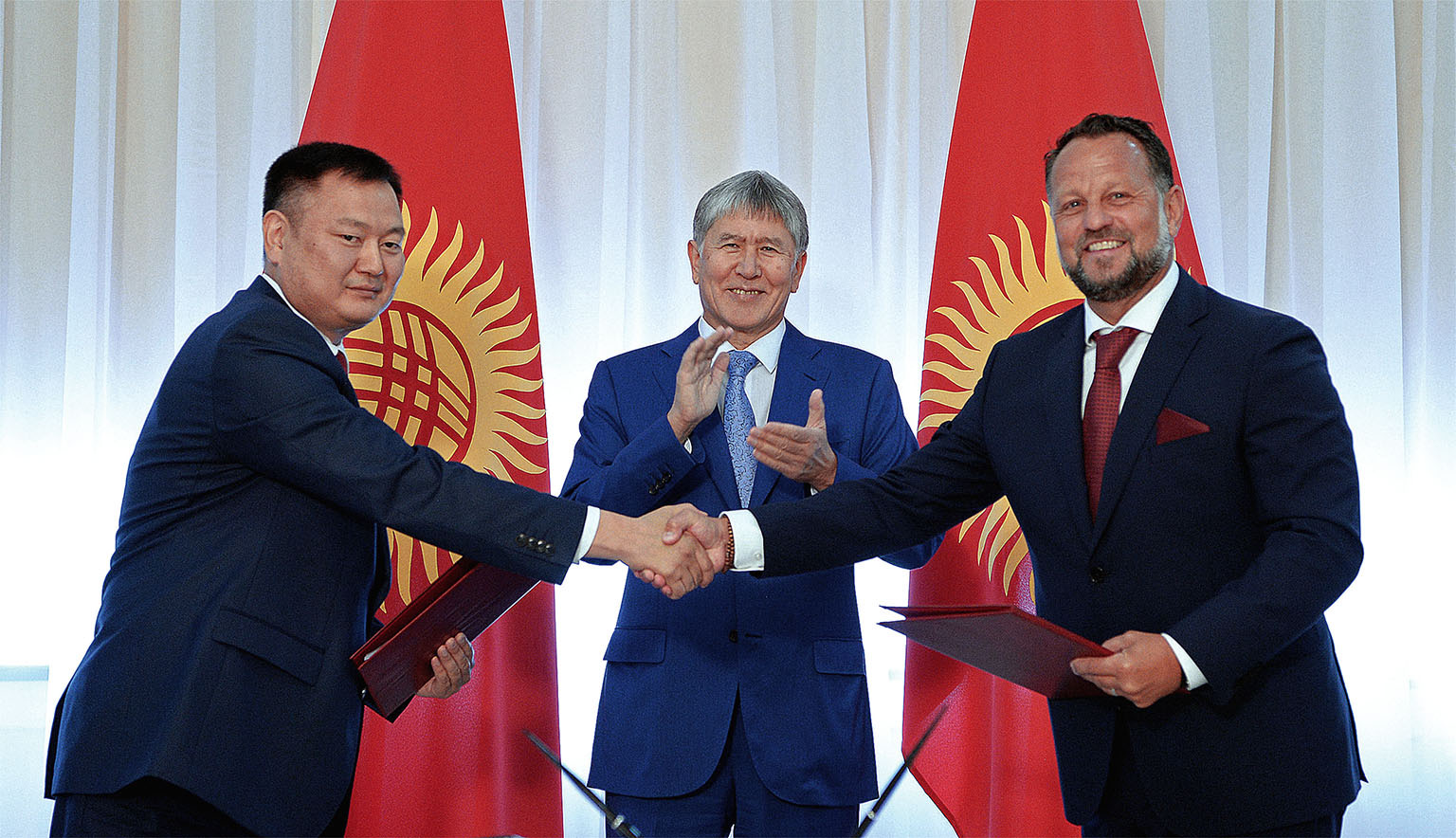 Smlouvu o výstavbě vodních elektráren za kyrgyzskou vládu podepisoval šéf přes energetiku Dujšenbek Zilalijev (vlevo). Třese si rukou s majitelem Liglass Trading Michaelem Smelíkem, uprostřed kyrgyzský prezident Almazbek Atambajev.