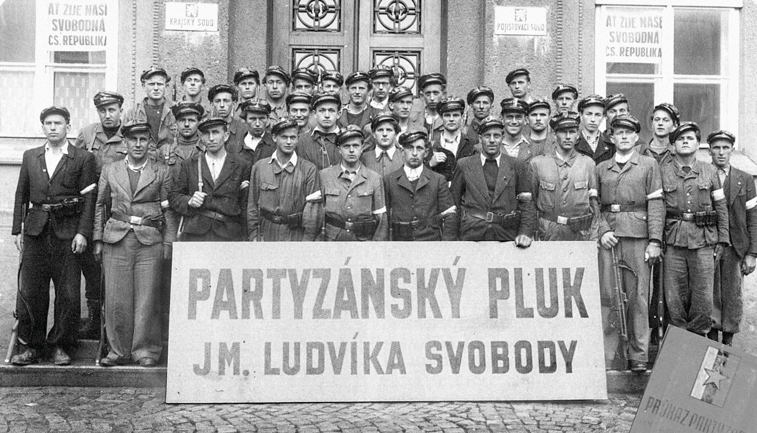 Na fotografii vlevo je čtvrtý zprava (s puškou v ruce) zachycen jednatřicetiletý desátník Jaroslav Pudil, který partyzánům velel.